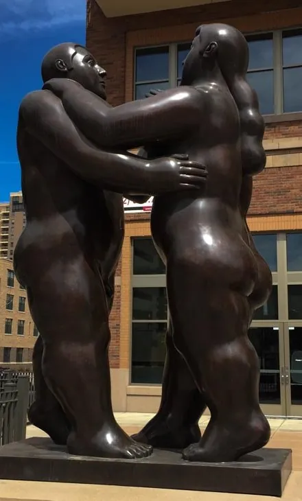 Bronze sculpture of two embracing figures outside a brick building