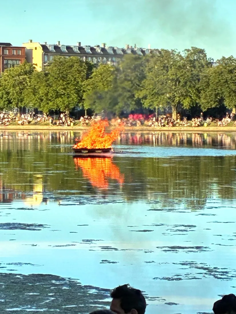 Fire burning on a raft on a city lake at sunset